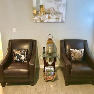 A cozy seating area with two leather chairs, decorative pillows, a small side table, and artwork on the wall.