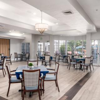 A spacious and well-lit dining room featuring multiple tables and chairs, with large windows allowing natural light to brighten the space.