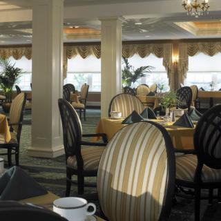 A sophisticated dining room with elegantly set tables and striped chairs, illuminated by a chandelier.