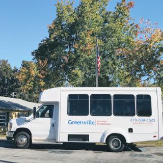 A white bus parked under colorful autumn trees, displaying an American flag.