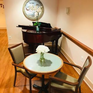 A cozy corner featuring a small table with chairs and a piano in the background, creating an inviting space for conversation and music.
