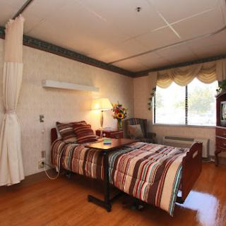 A cozy hospital room featuring a bed with striped bedding, a bedside lamp, and natural light coming through the window.
