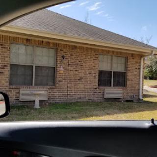 A view of a brick house with two front windows and an open lawn.