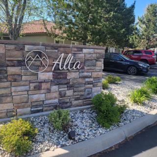 A stone sign with the word 'Alta', surrounded by landscaping and parked cars.