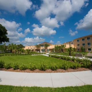 A well-maintained garden with a pathway, surrounded by a modern building under a partly cloudy sky.