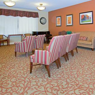 A cozy living room with striped chairs, a sofa, patterned carpet, and framed artwork on the walls.