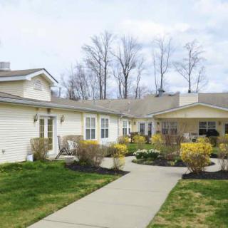 A view of a residential house with a well-maintained yard and pathway, surrounded by trees.
