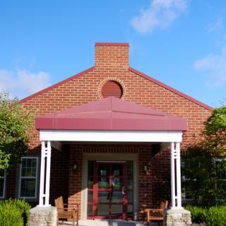 A brick building with a covered entrance and red roof under a clear blue sky.