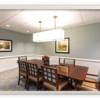 A well-lit dining room with a rectangular table and eight chairs, adorned with framed artwork on the walls.