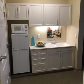 A compact apartment kitchen with white cabinets, a microwave, and a small fridge.
