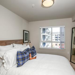 A modern bedroom with a neatly made bed, decorative pillows, and a large window offering natural light.