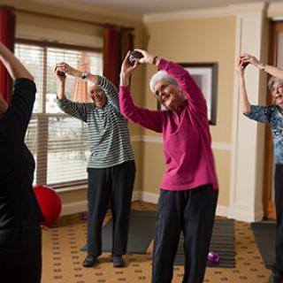 A group of seniors participating in a fitness class indoors, practicing stretching exercises together.
