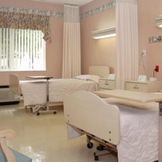 A clean and well-organized hospital room with two beds, privacy curtains, and medical equipment.