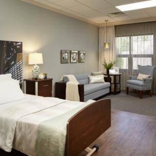 A modern and well-furnished hospital room with a patient bed, sofa, and seating area.