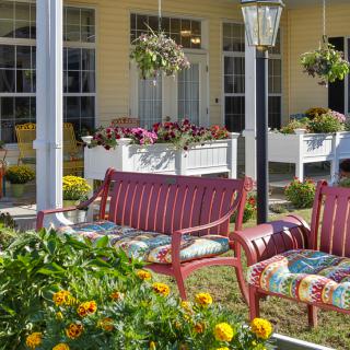 A cozy garden with colorful flowers and red patio furniture in front of a yellow house.