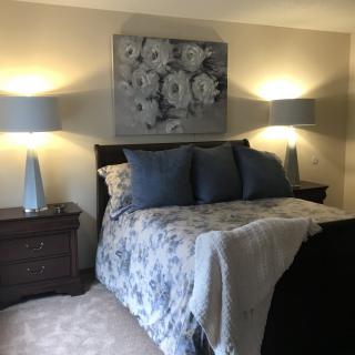 A cozy bedroom with decorative pillows, bedside lamps, and floral artwork above the bed.