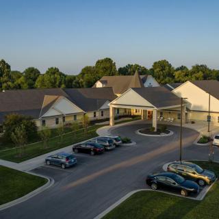 Aerial view of a building with a parking lot and cars, surrounded by trees at sunset.