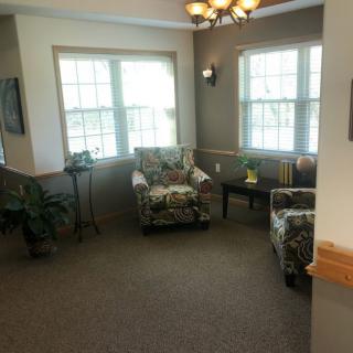 A cozy living room with two patterned chairs, large windows, and indoor plants.