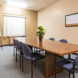 A neatly arranged conference room equipped with a wooden table and comfortable chairs, ready for discussions.