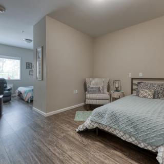 A modern bedroom with wooden flooring, featuring a cozy bed and a comfortable chair near the window.