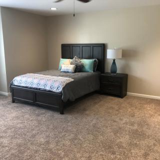 A modern bedroom with a neatly made bed, nightstand, and lamp on a carpeted floor.