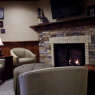 A cozy living room featuring a stone fireplace, comfortable armchairs, and a TV mounted above.