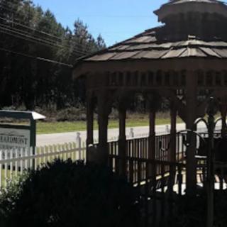 A gazebo by the roadside with a sign and trees in the background.