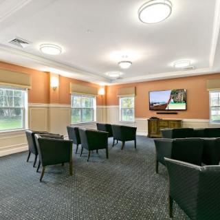 A conference room with multiple chairs facing a television, featuring large windows and bright lighting.