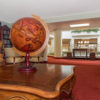An elegant library interior featuring a globe on a wooden table, surrounded by bookshelves and comfortable seating.