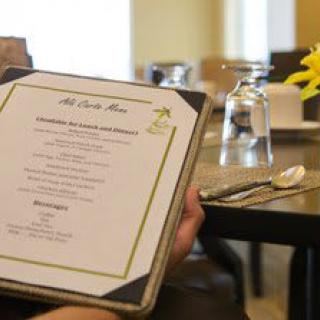 A person holding a menu in a restaurant with a table set elegantly with glasses, cutlery, and flowers.