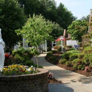 A serene garden pathway with lush greenery and a statue.