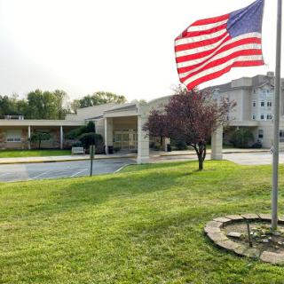 A view of a building with an American flag waving in the foreground, surrounded by a well-maintained lawn.