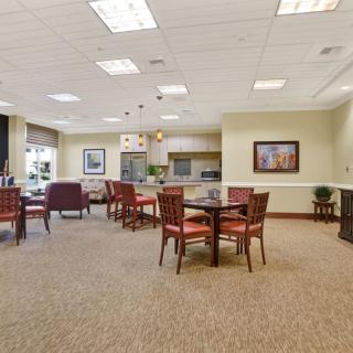 A spacious dining area with multiple tables and chairs arranged on a carpeted floor, well-lit by ceiling lights.