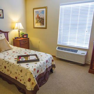 A cozy bedroom with a single bed, bedside table, and window with blinds.
