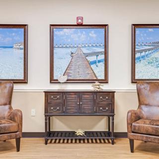 A stylish living room featuring three coastal-themed paintings above a wooden console table, flanked by two leather armchairs.