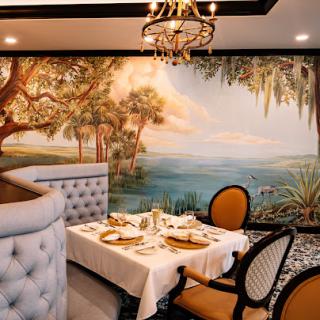 A beautifully designed restaurant interior featuring a scenic wall mural, elegant furnishings, and a cozy dining atmosphere.