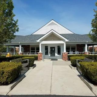 A symmetrical building with a central entrance, surrounded by neatly trimmed hedges and trees along a paved walkway.