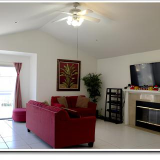 A cozy living room with a red sofa, television above a fireplace, and tasteful decor including a potted plant.