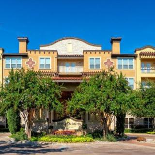 A residential building with a prominent entrance and surrounding greenery under a clear blue sky.