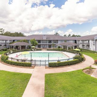 A scenic view of an apartment complex with a central swimming pool surrounded by landscaped greenery and pathways.