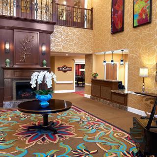 A stylish hotel lobby featuring a vibrant carpet, elegant floral arrangement on a central table, and cozy seating near the reception desk.