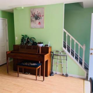A cozy living room featuring a piano and bench against a green wall, with stairs visible in the background.