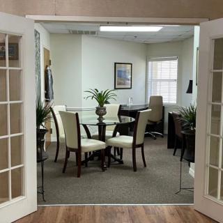 A cozy meeting room with a round table and chairs, decorated with plants.