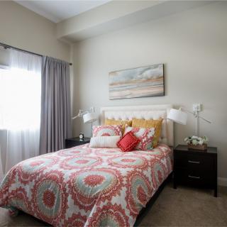 A cozy bedroom featuring a bed with patterned bedding and decorative pillows, accompanied by bedside tables and an artwork piece on the wall.