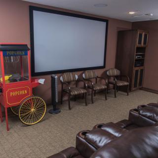 A cozy home theater setup featuring a large projector screen, comfortable leather couches, additional seating chairs, and a popcorn machine for an authentic movie experience.