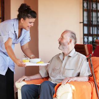 A caregiver serves a meal to an elderly man in a warm and inviting home setting.