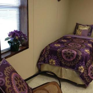 A cozy bedroom with purple-themed bedding and a chair by the window.