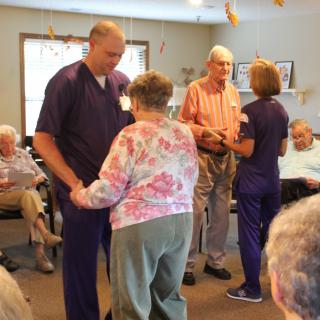 Elderly residents and caregivers dancing together in a nursing home.