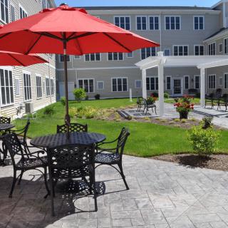 A modern outdoor patio area with tables, chairs, and red umbrellas overlooking a garden courtyard.