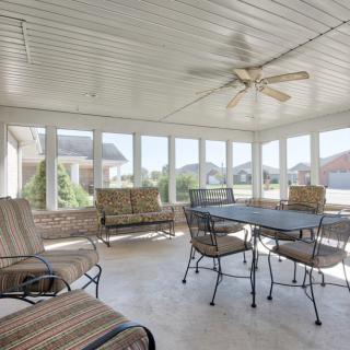 A bright enclosed patio with seating and a table, featuring large windows and a ceiling fan.